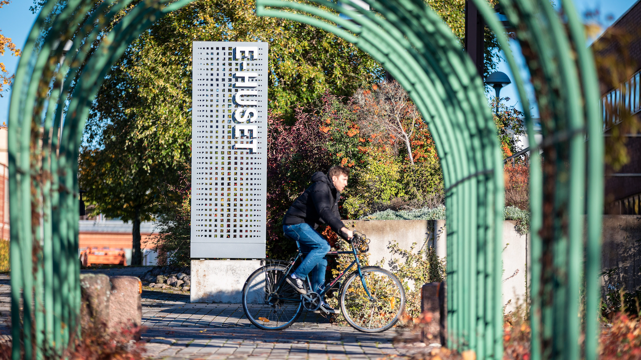 A student rides a bicycle past the E-Huset building sign at Linköping University
